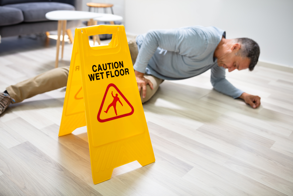mature man falling on wet floor in front of caution sign at home