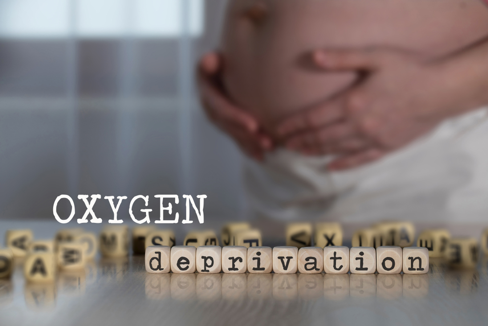 Words OXYGEN DEPRIVATION composed of wooden letters. Pregnant woman in the background